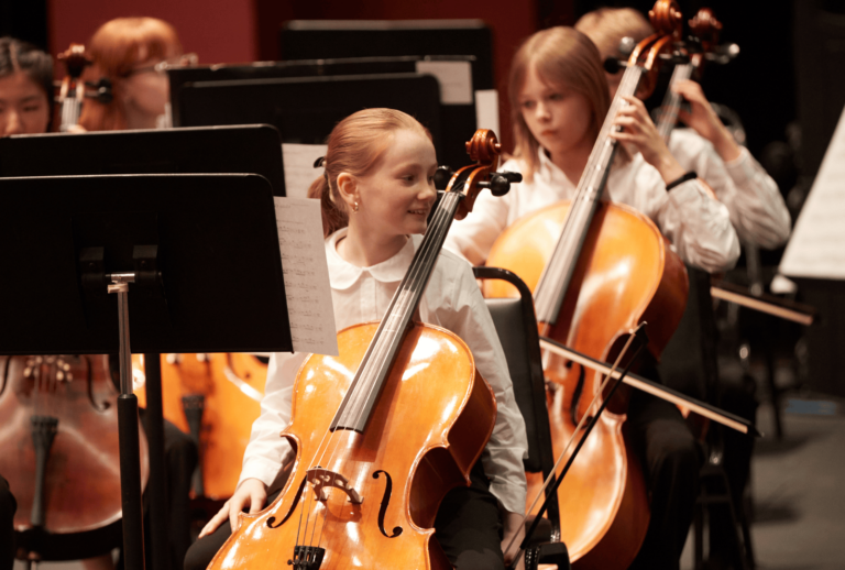 A smiling young student playing the cello